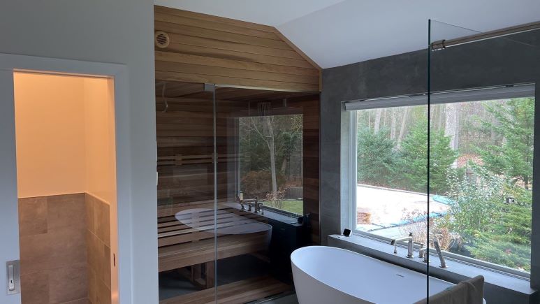 Glass walk-in shower beside a wood-lined sauna and freestanding tub in a remodeled bathroom